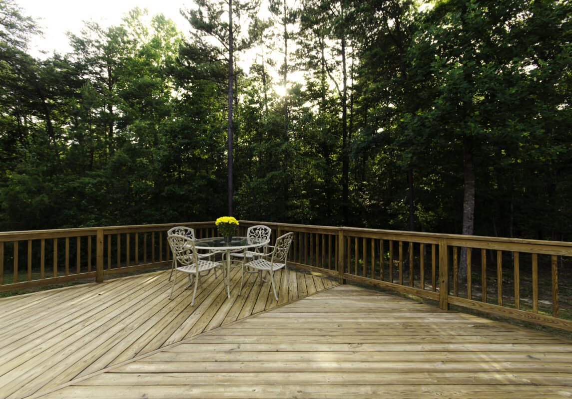 Natural pressure treated wood deck with classic wood railings and white metal dining set surrounded by lush green trees in Virginia