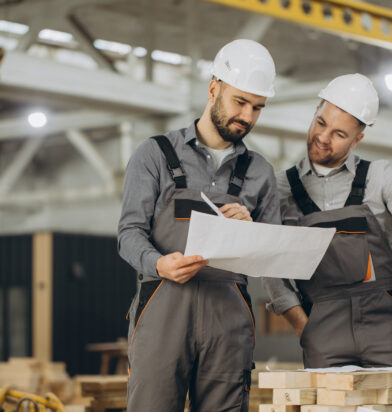 Two builders reviewing blueprints and preparing to assemble prefabricated components in a modular building factory